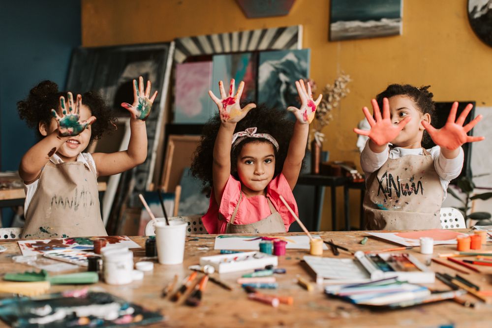 Three joyful children showing off their colorful painted hands in the art studio at Cre8tive Colorz